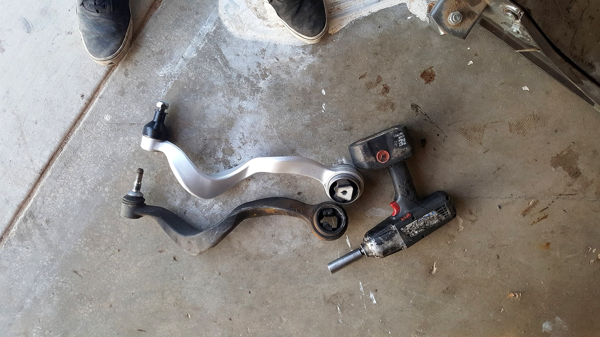 A removed control arm and an impact gun on the concrete